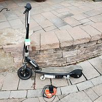 Side view of Razor electric scooter parked on stone pavement with charger placed next to rear wheel.