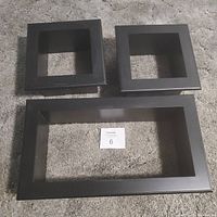 Three black framed wall shelves (two square, one rectangular) on carpeted floor showing front view.