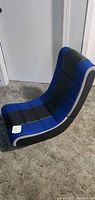 Side angle view showing the blue and black padded gaming chair on carpeted floor.