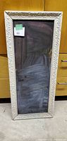 Full view of the tall rectangular chalk board showing black writing surface and decorative cream-colored embossed frame.