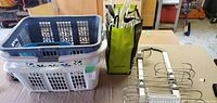Photo showing three plastic laundry baskets stacked with blue and white colors, and green/black tote bag with closet hangers beside an adjustable shower rack.