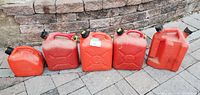 Five red plastic jerry cans arranged on paving stones in a single row showing various sizes from 1 gallon to 2.5 gallons. Caps visible, containers used with wear and scuffs.