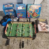 Full view of all lot items laid out on floor including the games Heist, Design Your Own Globe, Don't Step In It, Jumbling Tower, VR headset, and Mini Foosball table.