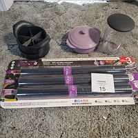 Full view of all items in kitchen lot including black chopper, lavender baking dish with lid, clear measuring container, and pack of three silicone oven liners.