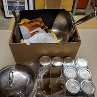 Top view of box containing wok with lid, cast iron grill pan, mason jars, and other items.