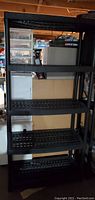 Full view of the assembled black plastic shelving unit with five ventilated shelves in a storage setting.