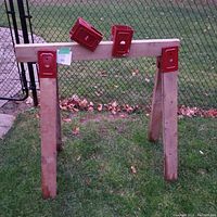 Full assembled saw horse clamps holding wood outdoors on grass near a chain link fence to show setup and item count.