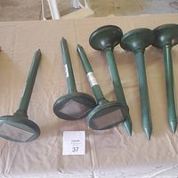Seven green pointed stakes with rectangular solar panels on top, laid out on a beige fabric surface.