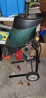 Green and black electric yard shredder with metal frame, wheels, handle, and chute, showing dirt and wear.