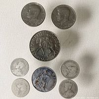 Top view of two American half dollar coins from 1972 and 1976, and British Jubilee token from 1977 plus five British coins including 1919 penny and four others in worn condition