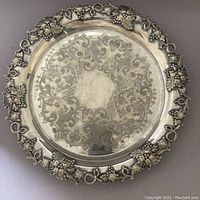 Top view of antique silver plate serving tray showing etched design and grape vine patterned rim.