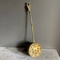 Full view of antique brass bed warmer showing long handle and circular warming pan.