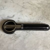 Top-down photo of the black leather sheath with white stitching and silver detail containing the scissors and letter opener.