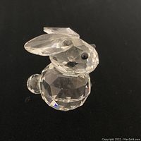 Clear Swarovski crystal rabbit figurine shown from side angle on black background, showing faceted body and black crystal eyes.