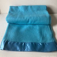 Folded vintage mineral blue wool blanket with satin border on a light surface.