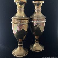 Pair of vintage brass candle holders shown against black backdrop, highlighting their reflective brass surfaces and embossed detailing on midsection.