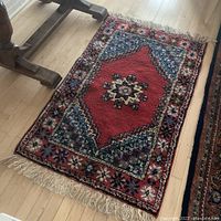 Full view of rectangular wool Persian style rug with red center medallion and blue floral border, showing fringe and floor beneath.