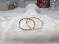 Two gold bangles side by side on white cloth background