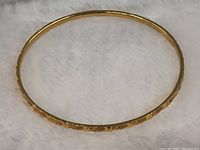 Full view of circular gold bangle on white background