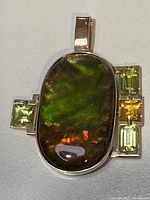 Front view of the oval ammolite doublet pendant set in 14K yellow gold with peridot and citrine accents