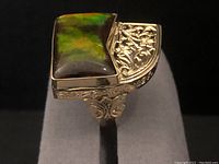 Front three-quarter view of ring on grey display stand showing stone color and filigree detail