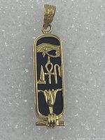 Front view of pendant showing gold cartouche frame, onyx inlay and raised hieroglyphs including Eye of Horus, ankh and lotus motifs