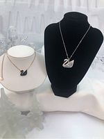 Two swan necklaces displayed side by side on white and black bust forms