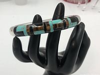 Front view of inlay pattern on polished silver bangle displayed on black hand stand