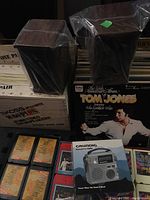 Two Koss Dynamite M/60 speakers on top of original boxes, also showing a Tom Jones vinyl album and a Grundig emergency radio box in the foreground