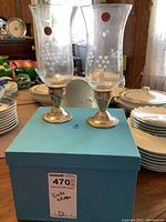 Pair of Birks sterling silver candle holders with etched crystal hurricane shades, displayed on a table with dishes and a blue box underneath labeled 'Birks silver' with lot number.
