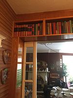 Books neatly arranged on a wooden shelf above a doorway in a wood-paneled room.