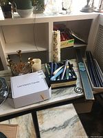 Overall view of items including brass candle holders, LED electric candle box, assorted candles, plate holders on marble surface and shelving unit.