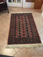 Full view of the wool rug laid out on a tile floor, showing the rug's pattern, color, and fringes.