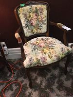Front view of the vintage upholstered chair showing floral fabric and wooden arms with wear on padding.