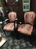 Two upholstered armchairs with dark carved wooden frames and patterned pink damask fabric upholstery. The chairs are placed side by side on a carpeted floor.