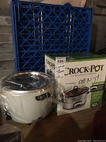 White rice cooker wrapped in clear plastic alongside the Crock-Pot box and stoneware crockpot.