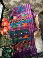 Colorful purple silk scarf with geometric and floral patterns folded on top of other fabrics.