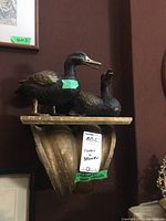 Two dark metal painted duck figures mounted on a decorative carved wood wall bracket with a scroll design.