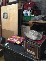 Photo of stacked items including pink Disney Princess Treasure Chest board game, storage trunk, and other boxes