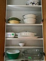 Photo showing three shelves filled with vintage ceramic and glass bakeware including Pyrex and Corningware casserole dishes, nested bowls and pie plates.