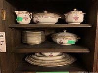 Full display of Limoges china including stacked plates, lidded dishes, cream pitcher, and platters on wooden shelves