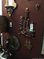 Musical-themed metal wall art and Asian-style trivet with swan trinket on reddish wall, brass decorative plate nearby.