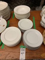 Three stacks under green tape: plain white plates (left), silver-rim plates (right), soup bowls (center)
