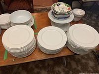 Two large stacks of wrapped white dinner plates and some bowls on a table.