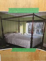 Photo of the assembled queen size four-poster bed in a bedroom, showing carved wooden posts and a canopy frame.