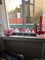 Wide view of assortment on window ledge showing multiple red and pink glass bowls, cordial glasses, and tall vases.