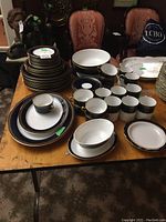 Full display of the assortment of Romanov china pieces including plates, cups, mugs, serving bowls and platters spread on a wooden table.