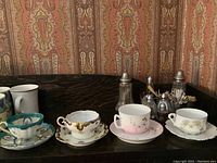Four antique Royal Doulton teacups and saucers with varied floral patterns lined up on a dark surface against a patterned wall.