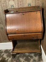 Front and angled views of vintage oak veneer secretary desk showing damage to front veneer, carved lion feet, drawer with two handles, bottom and top shelves, and key on drop-front writing surface.