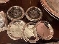 Two round silver plate dishes and four silver plated coasters on a dark wooden surface